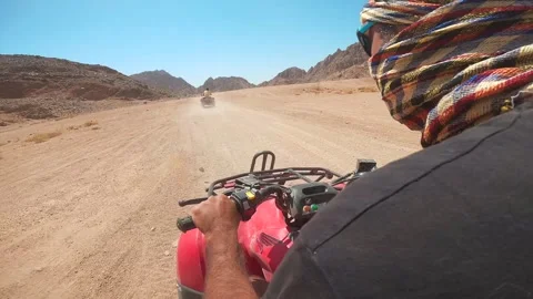 Side close up view of man in keffiyeh driving fast atv bike in the wild desert Stock Footage 252382026