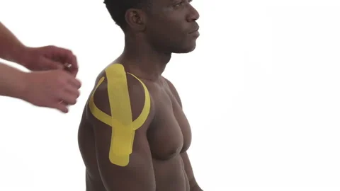 Side close-up view of a therapist removing yellow tape from athletic male Video stock 133770649
