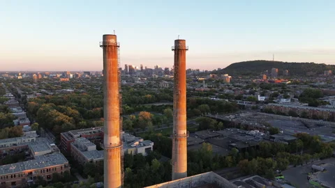Side drone pan of industrial chimneys with Montreal skyline at sunset Stock Footage 317558244