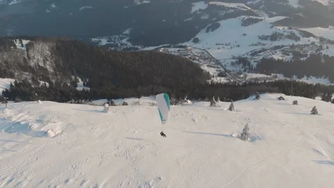 Side Drone Shot Of Tandem Paraglide Landing On Snow Covered Mountains Vídeo Stock 149201456