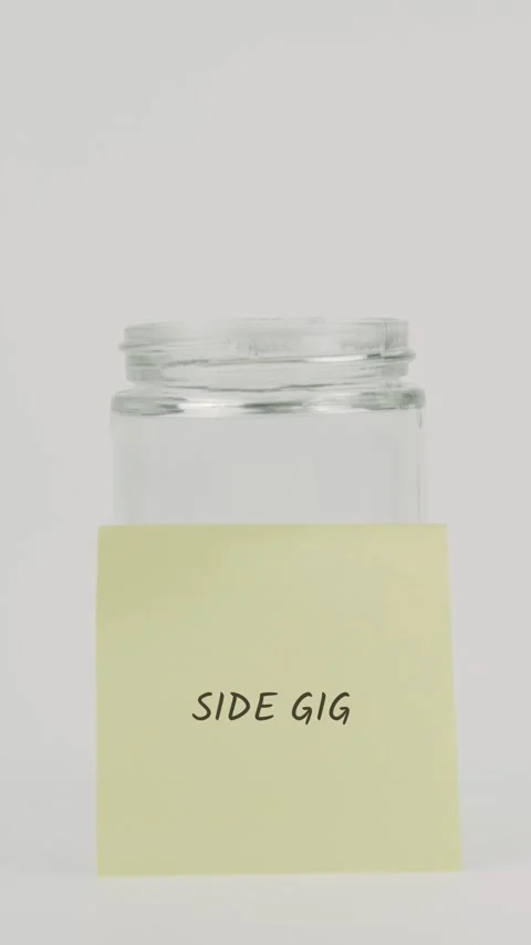 Side gig text or word on yellow sticky note attached to glass jar with hand Stock Footage 311786414