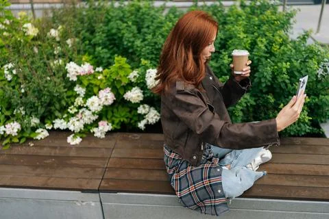 Side high-angle view of pretty woman with red hair sitting on bench, taking Stock Photos