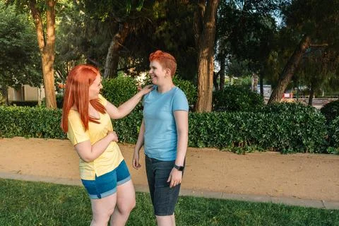 Side image of two friends laughing intensely, in a city public park at sunset Stock Photos