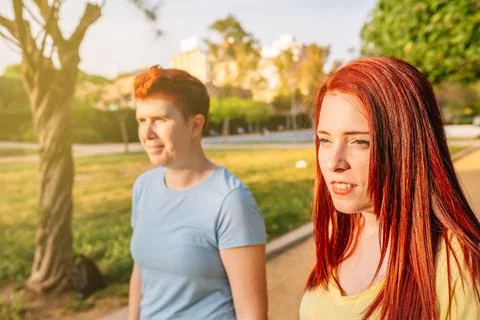 Side image of two young friends walking carefree in a public park at sunset Stock Photos