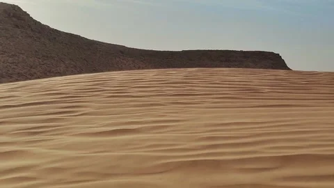 Side-lit Sahara dune slope rippled by wind, distant mesa anchoring the frame  Stock Footage 344530350