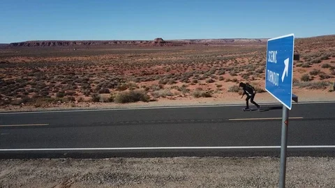 Side on Man Skate Boarding Down Desert Highway Drone Follow Stock Footage 99096309