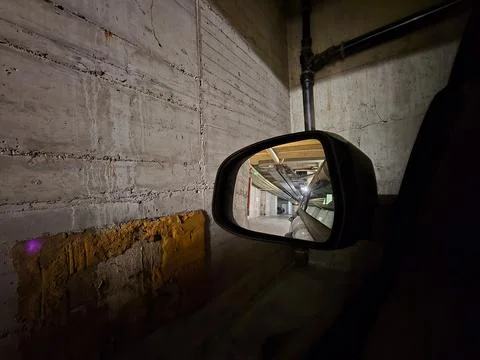 Side mirror of a car reflecting a lower parking lot in a large building Stock Photos