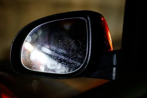 Side-mirror with raindrops and reflection on car at night while driving Stock Photos