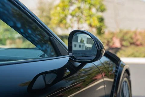Side mirror reflection showing a closer view of objects on a black car. Stock Photos