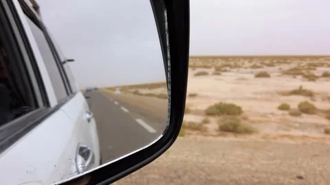 Side mirror view of a car driving on a road in Sahara desert Stock Footage 305505790