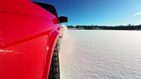Side-mounted action shot of a red car drifting on a frozen lake, kicking up Vídeo Stock 331488010