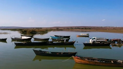 Side move over a lake by passing fishing boats, a red tractor and migratory peli Stock Footage 119601408