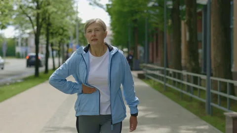Side pain while running. Mature woman runner is walking down the street after Stock Footage 226612055