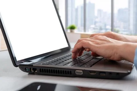 Side perspective of hands typing on laptop mockup in bright office interior.. 库存照片
