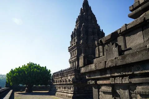 Side perspective of a Prambanan Temple tower beside a sunlit stone walkway .. Stock-Fotos