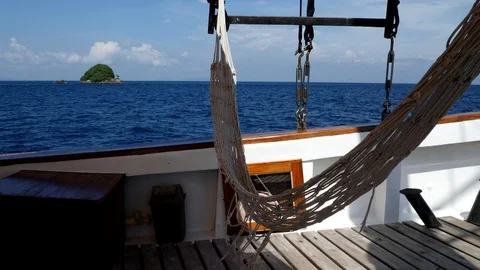 Side of phinisi boat with hammock floating with the wind, island behind Stock Footage 112483626