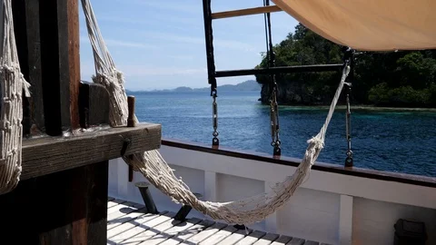 Side of phinisi boat navigating with hammock hanging, island behind Video stock 112483783