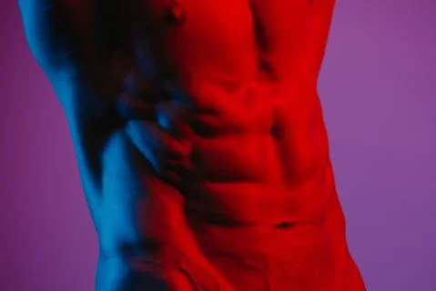 A side photo of the abs of a bodybuilder under blue and red lights. Stock Photos