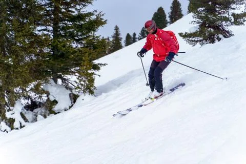 Side photo of sports man in red jacket and with backpack skiing in winter resort Stock Photos