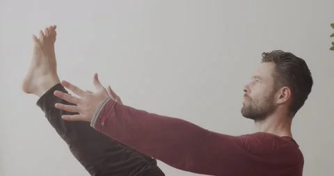 Side portrait of bearded man balancing in seated asana pose indoors on white Stock Footage 141179330