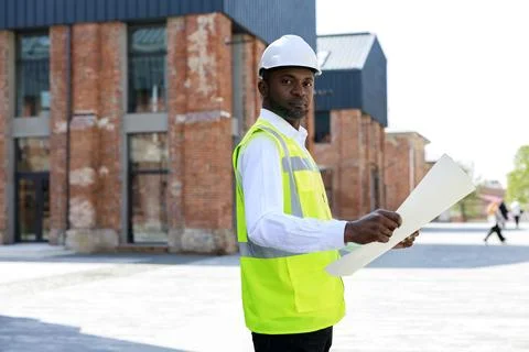 Side portrait of the engineer wearing white helmet and holding building project Stock Photos