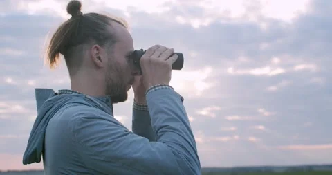 Side portrait of explorer looking into binoculars on nature sunny sky background Stock Footage 135249594
