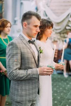 The side portrait of the newlyweds holding the decorated candles in the church. Stock Photos