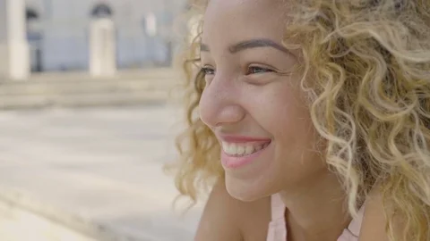 Side portrait of a young blonde curly woman smiling outdoor in the city Stock Footage 80543353