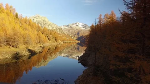 Side POV walking on fall woods path near lake and trees with snowy mounts.Sunny Видео 80091036