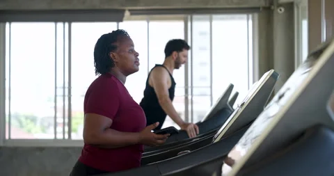 Side profile of African American plus size woman running on treadmill, breathing Stock Footage 342584801