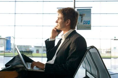Side profile of a businessman using a laptop and talking on a mobile phone at an Stock Photos