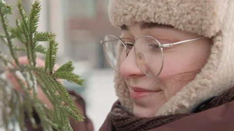 Side profile closeup of person in knit hat and glasses leaning toward evergreen Stock Footage 343545846