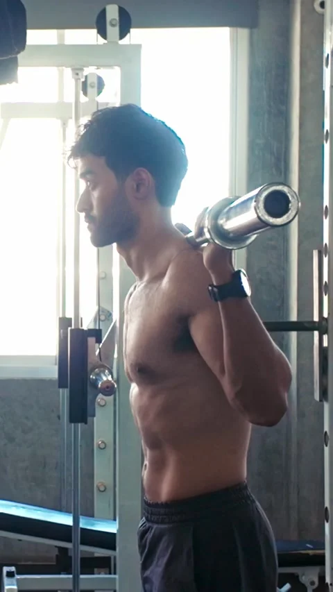 Side-profile of a man performing a barbell back squat in a gym, focused on .. Stock Footage 347733625