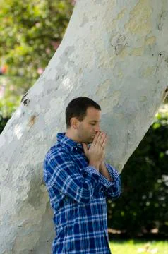 Side profile of a man praying alone by a tree trunk. Stock Photos