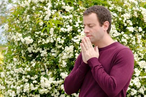 Side profile of man praying in front of a flowering bush. Stock Photos
