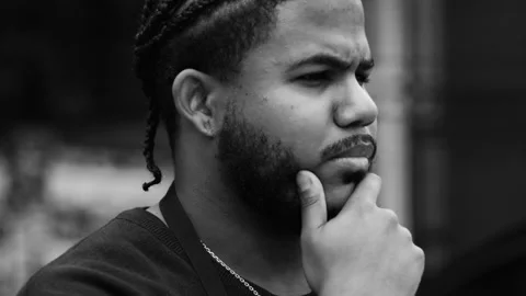 Side profile of a pensive black man with braided hair resting hand on chin, cont Vídeo Stock 319570109