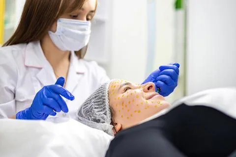 Side profile picture of a dermatologist executing a skin treatment to a client Stock Photos
