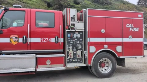 Side profile of a red CAL FIRE wildland engine parked near forested hills Stock Footage 348038765