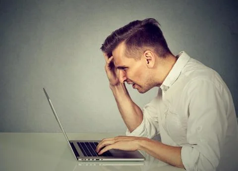 Side profile stressed man working on laptop sitting at table Stock Photos