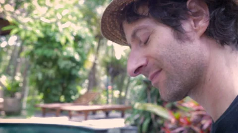 Side profile view of a young man playing a ukulele by an infinity pool Stock Footage 57807105