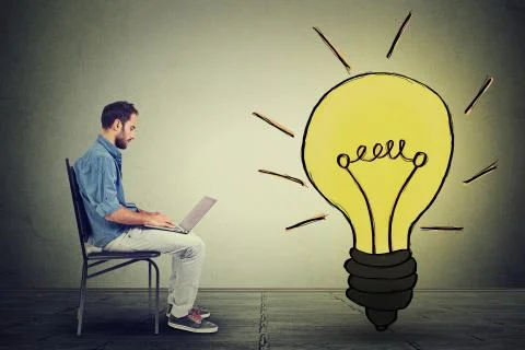 Side profile young man using laptop with light bulb on gray wall background Stock Photos