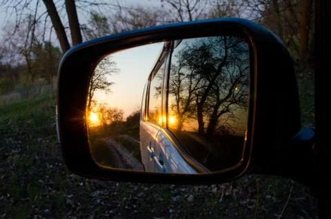 Side rearview mirror of car with reflection of beautiful sunset in the forest Stock Photos