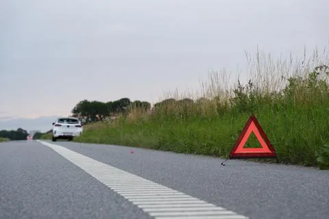 At the side of the road is a warning triangle, behind it a white car with a.. Stock Photos