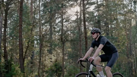 Side shot of cyclist riding a road bike in a sunny forest, wearing helmet Vídeo Stock 166174173