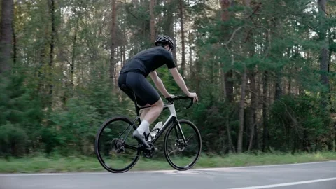 Side shot of cyclist riding a road bike in a sunny forest, wearing helmet 스톡 동영상 166174229