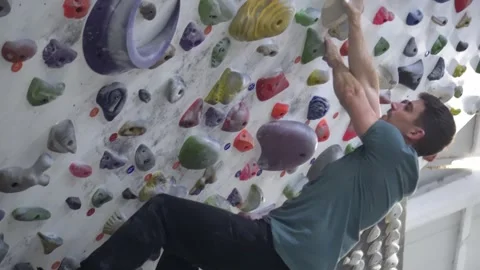 Side shot of a man climbing on an artificial climbing wall inside a climbing gym Stock Footage 255433250