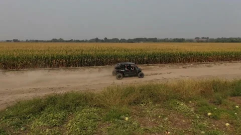 Side by side ATV drives along dirt farm roads next to corn field fast aerial Video stock 167856184
