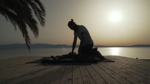 Side silhouette view of masseur doing thai yoga massage for a woman at sunrise Stock Footage 130794131