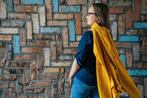 Side view of a 40-year-old woman in glasses against a colorful brick wall Stock Photos