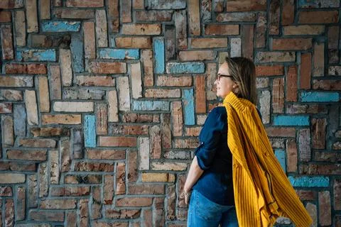 Side view of a 40-year-old woman in glasses against a colorful brick wall Stock Photos